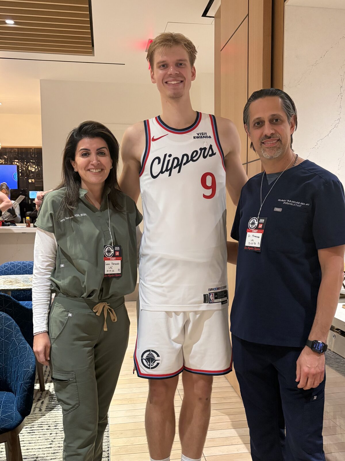 Dr. Homan Hanasab and Sanaz Hanasab in scrubs with an LA Clippers player in uniform at the team facility