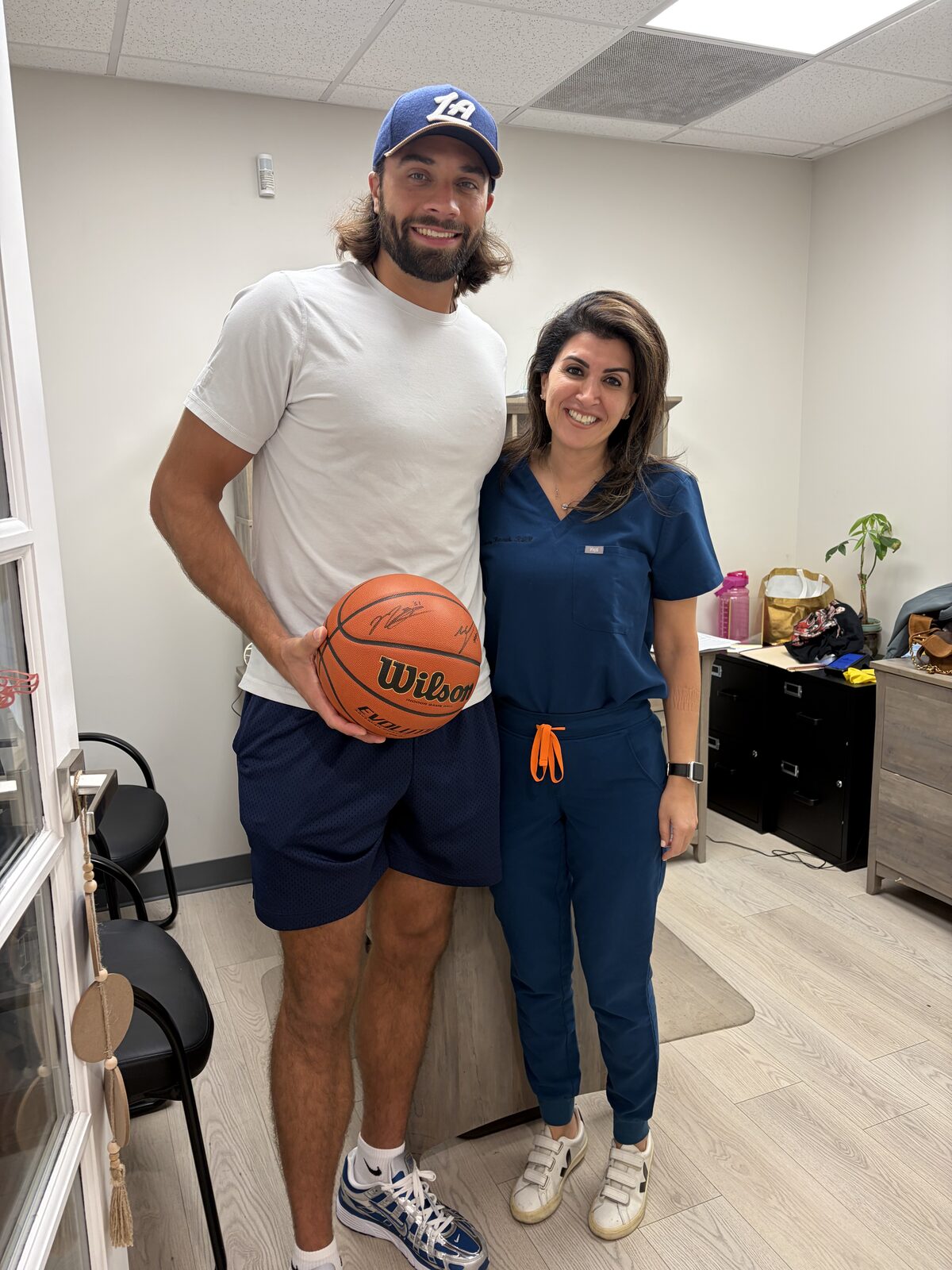Sanaz Hanasab with an LA Clippers player holding a signed basketball at American Dental Group