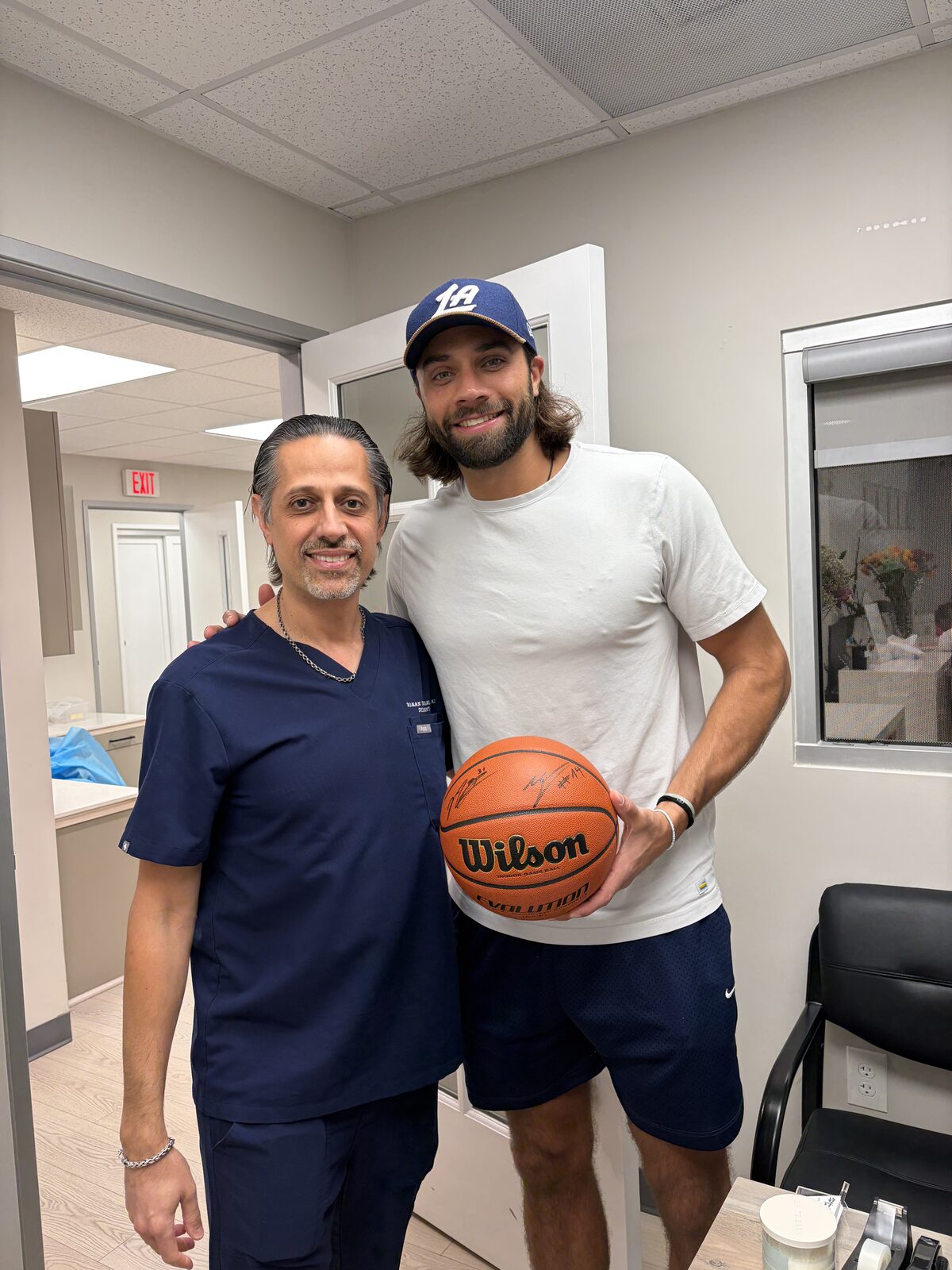 Dr. Homan Hanasab with an LA Clippers player holding a signed basketball in the American Dental Group office