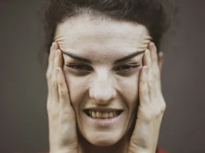 Woman pressing both hands to her jaw and temples in discomfort, a typical presentation of TMJ pain