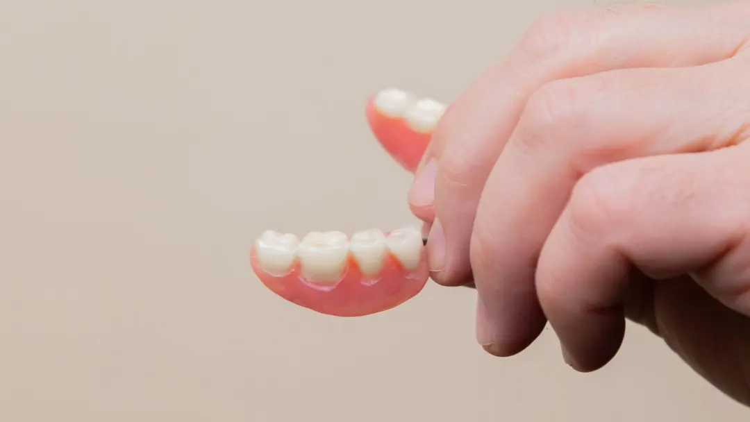 Hand holding a removable partial denture, one of the tooth replacement options compared with implants