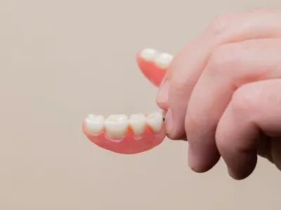 Hand holding a removable partial denture, one of the tooth replacement options compared with implants