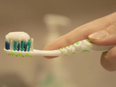 Hand holding a toothbrush with a pea-sized amount of toothpaste applied to soft bristles