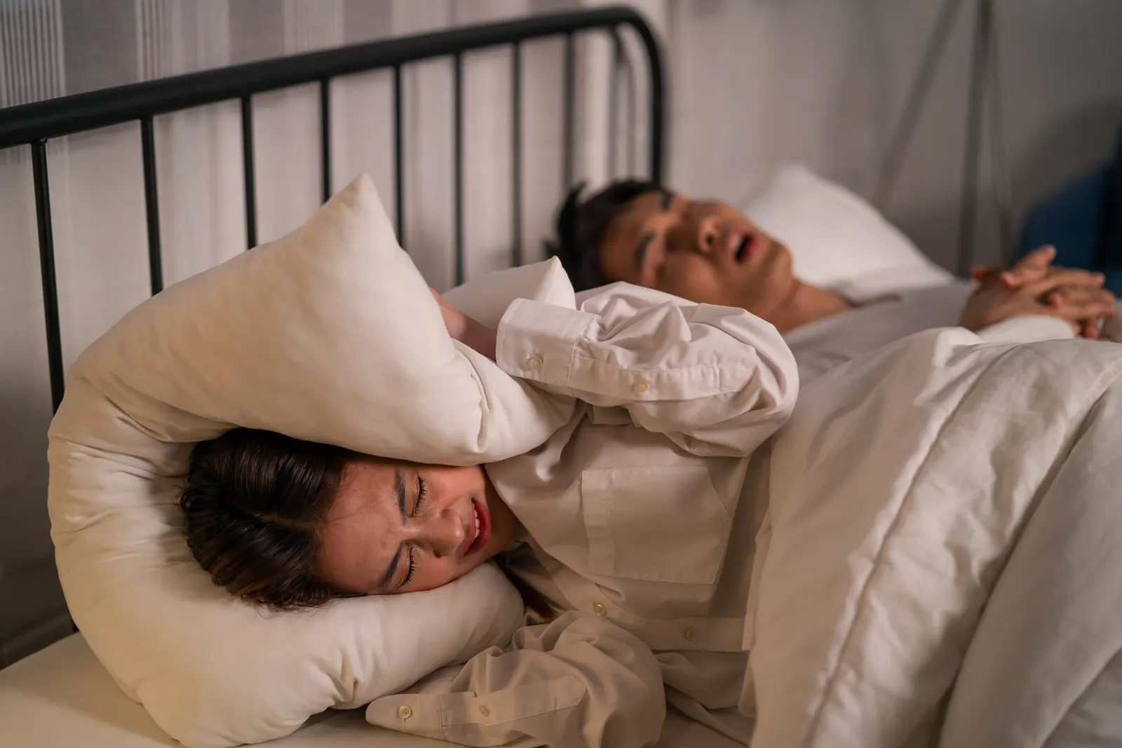 Woman covering her ears with a pillow while her partner snores — the hidden health risks of snoring in West Covina
